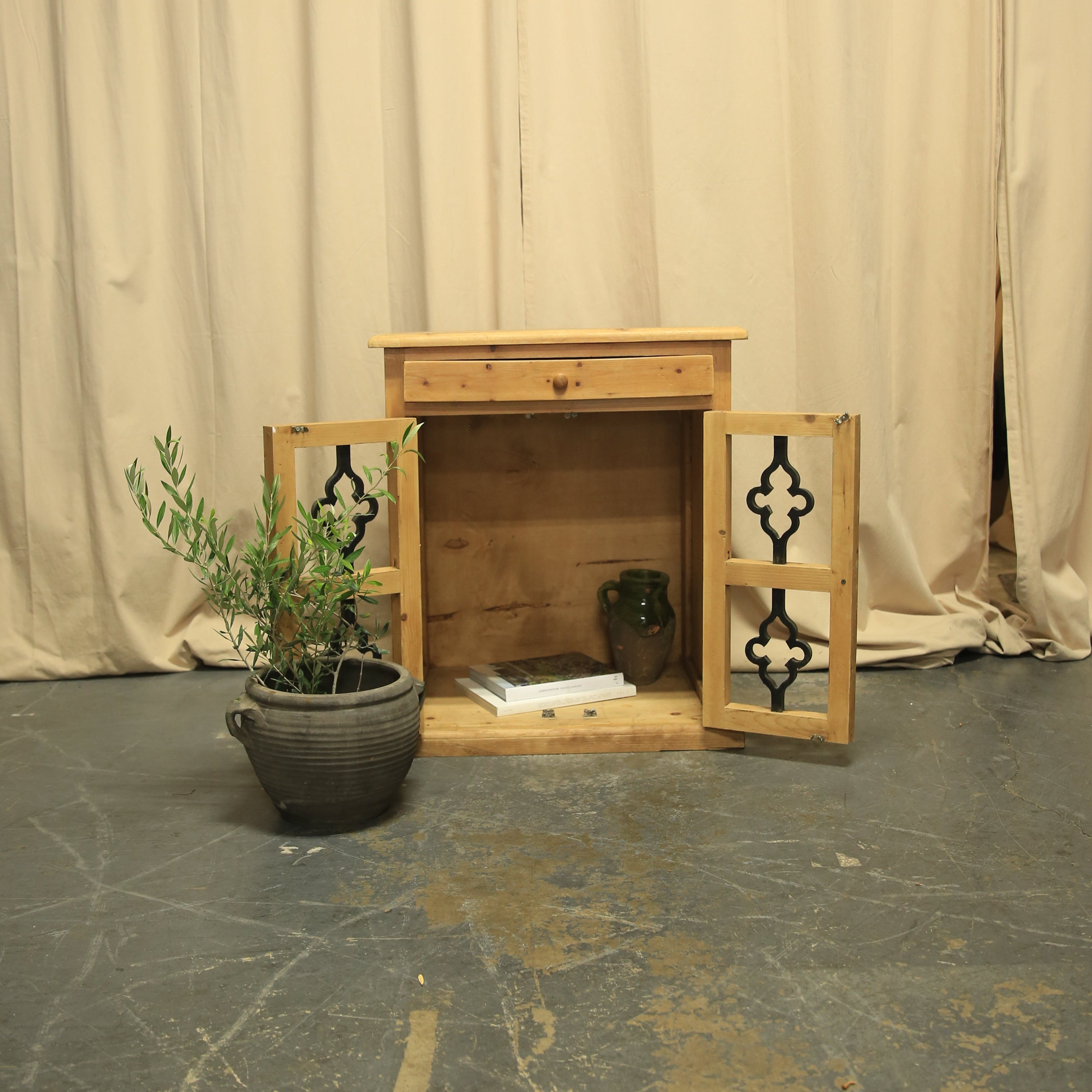 Wooden side table with two drawers and a plant on a textured floor and wall.