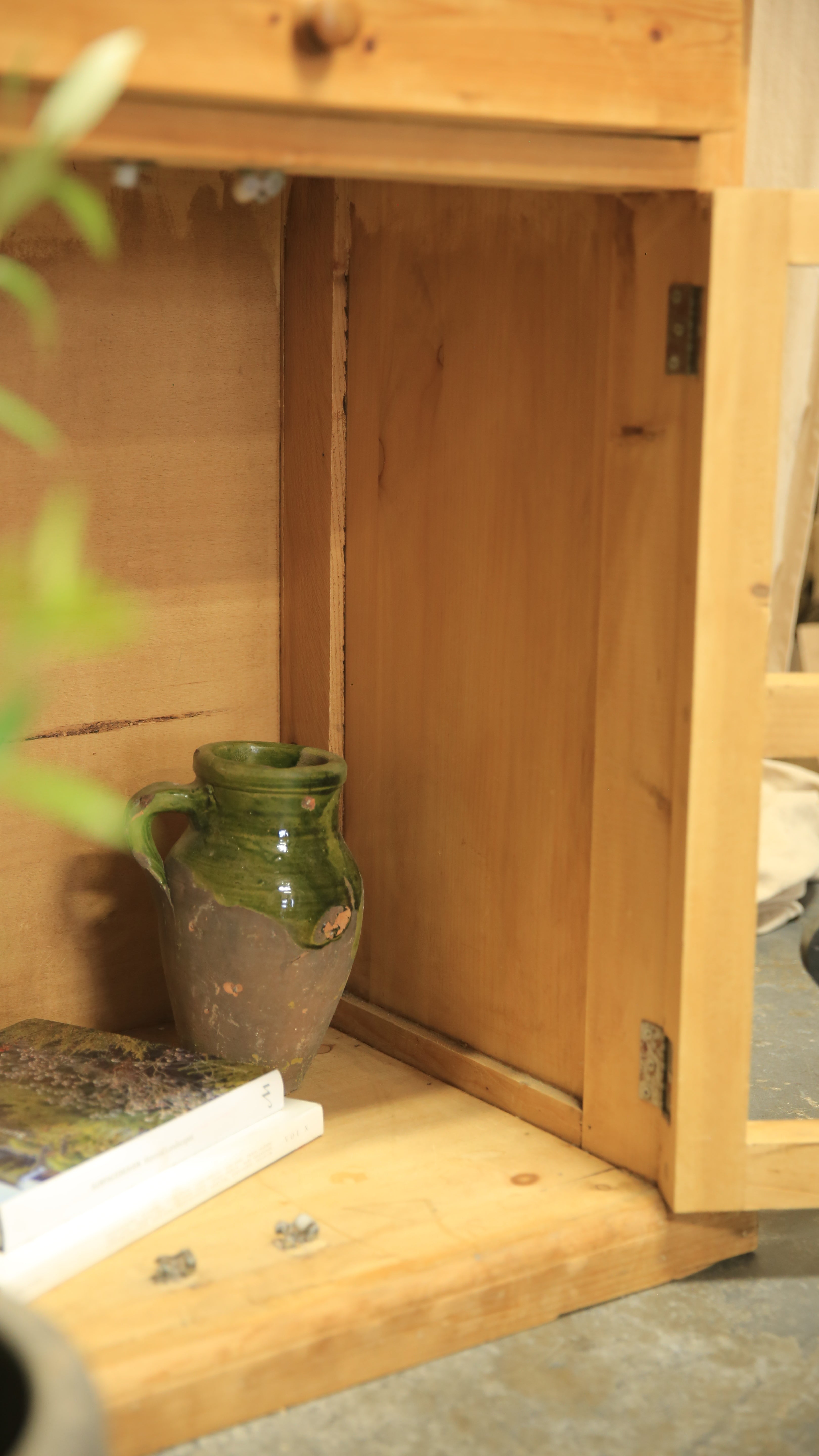 Green ceramic vase on a wooden shelf with a blurred background
