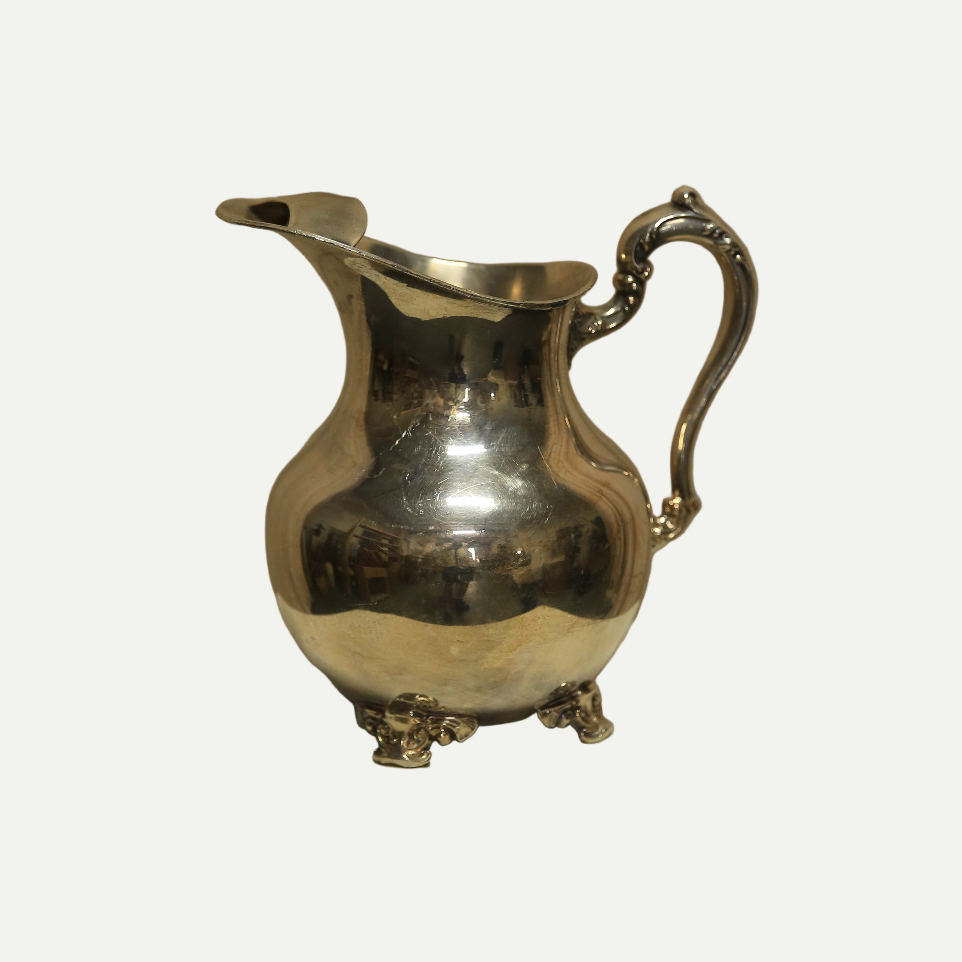 Silver pitcher on a white pedestal against a beige background