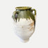 Vintage ceramic vase with green glaze on a dark floor with wooden shelves in the background.