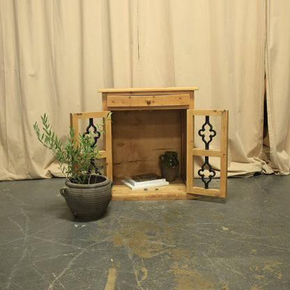 Wooden side table with two drawers and a plant on a textured floor and wall.