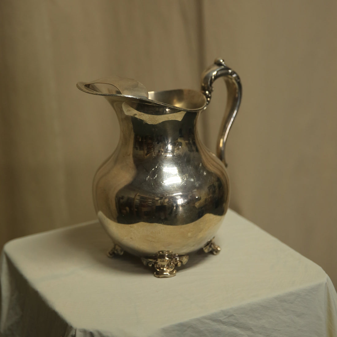 Silver pitcher on a white surface with a beige background