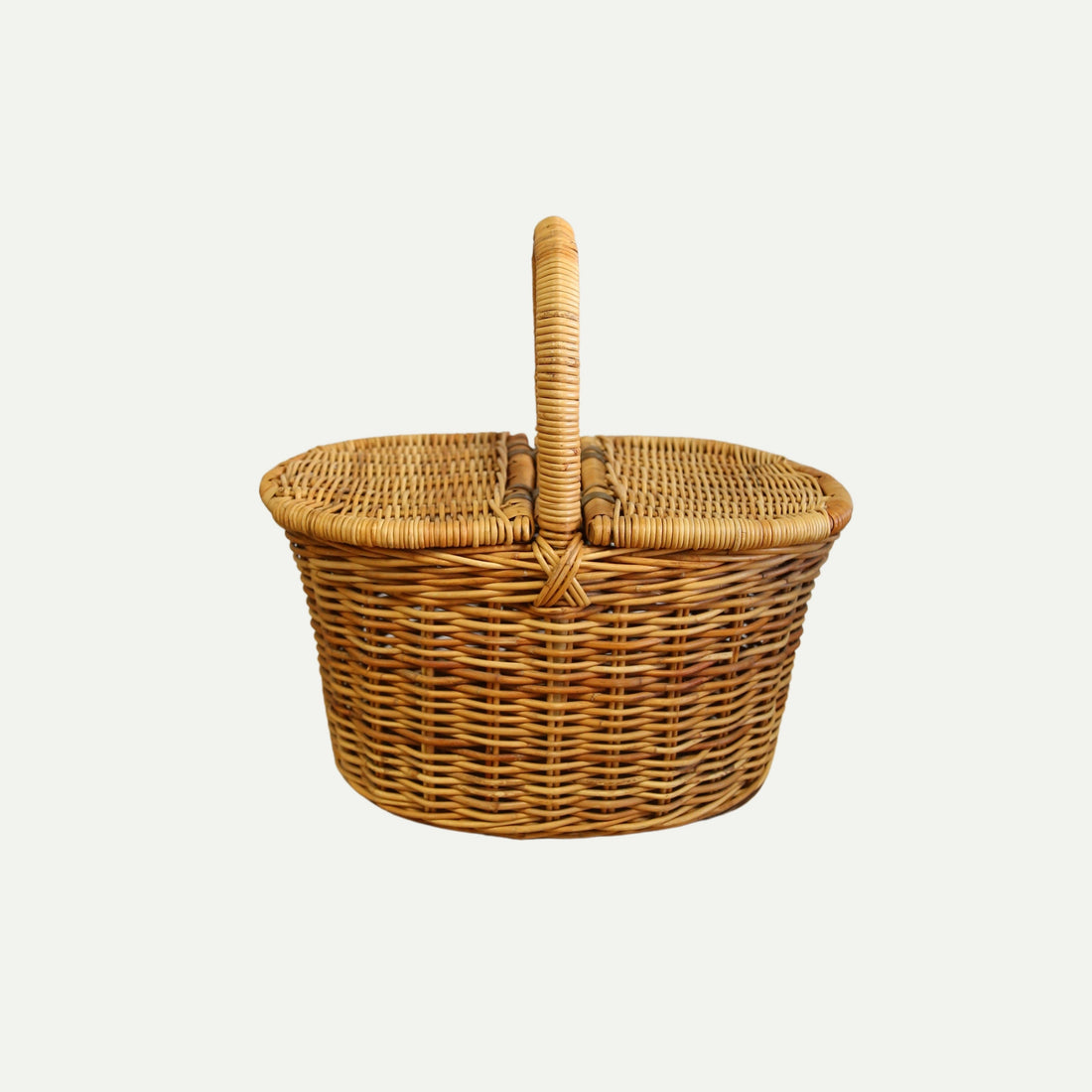 A handwoven wicker picnic basket with a rounded shape, dual flip-top lids, and a sturdy arched handle, shown against a plain light background.