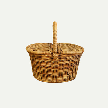 A handwoven wicker picnic basket with a rounded shape, dual flip-top lids, and a sturdy arched handle, shown against a plain light background.