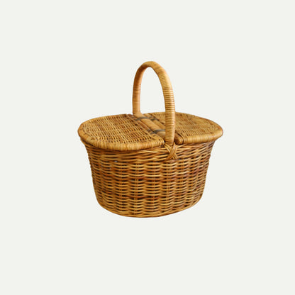 A handwoven wicker picnic basket with a rounded shape, dual flip-top lids, and a sturdy arched handle, shown against a plain light background.