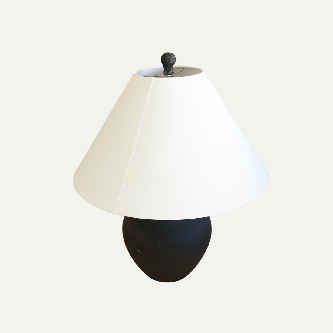 Table lamp with a matte black ceramic base shaped like a vintage amphora and a wide, off-white conical lampshade, set against a plain light background.